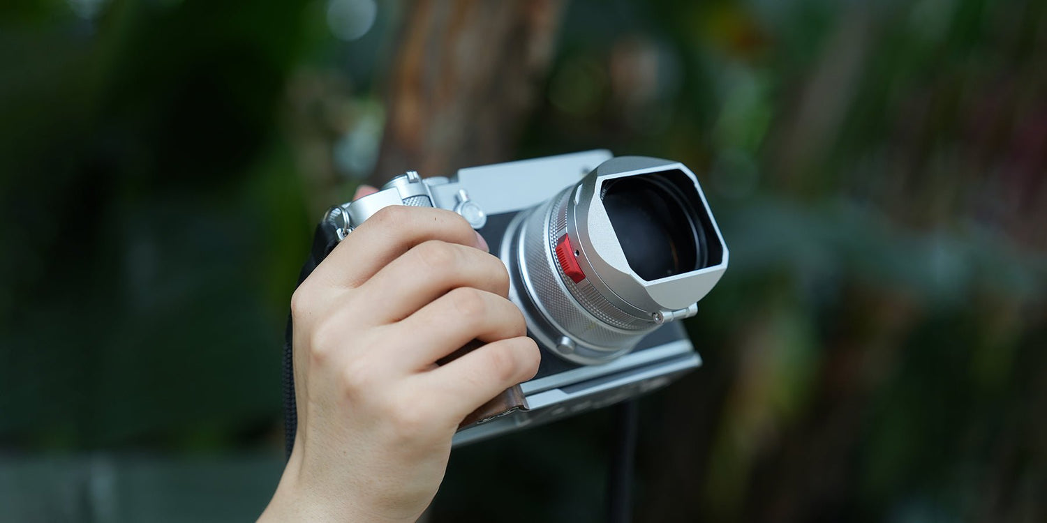 Fujifilm GF100RF camera fitted with Lens Hood in black, showcasing touchless filter ring and hands-on use in bright daylight.