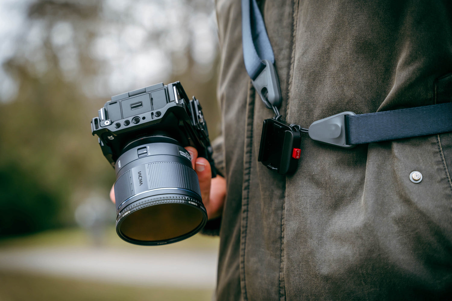 Person holding a camera with a Freewell strap attached to their side, showing the camera's lens and strap mechanism.