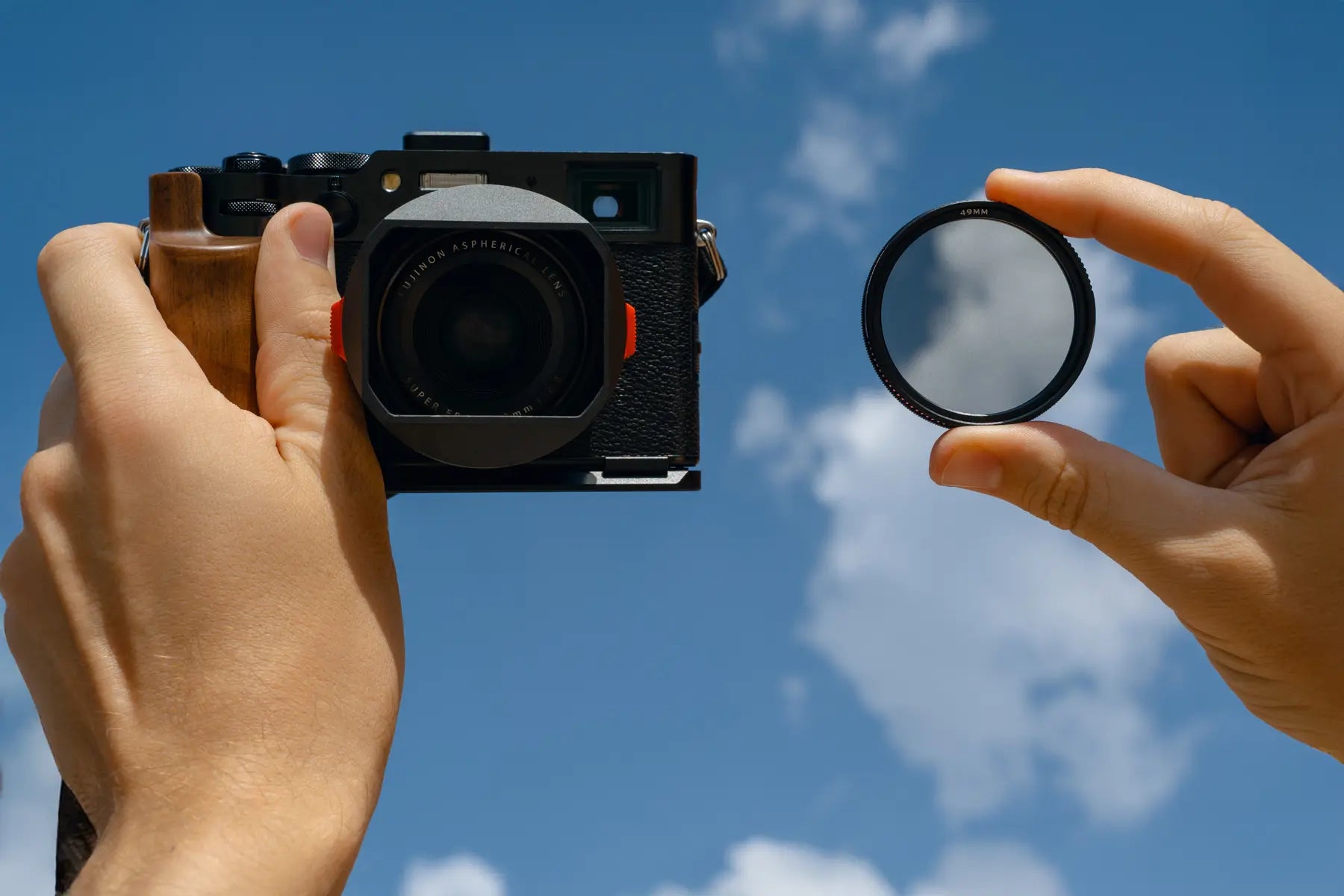 Fujifilm X100 camera and filter held against a blue sky